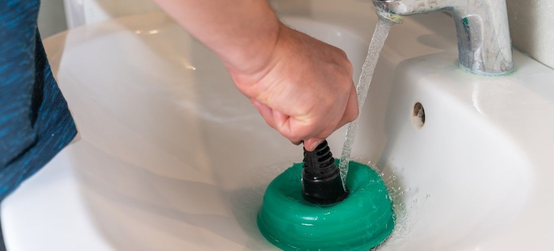 Plumber unclogging sink with a green plunger.