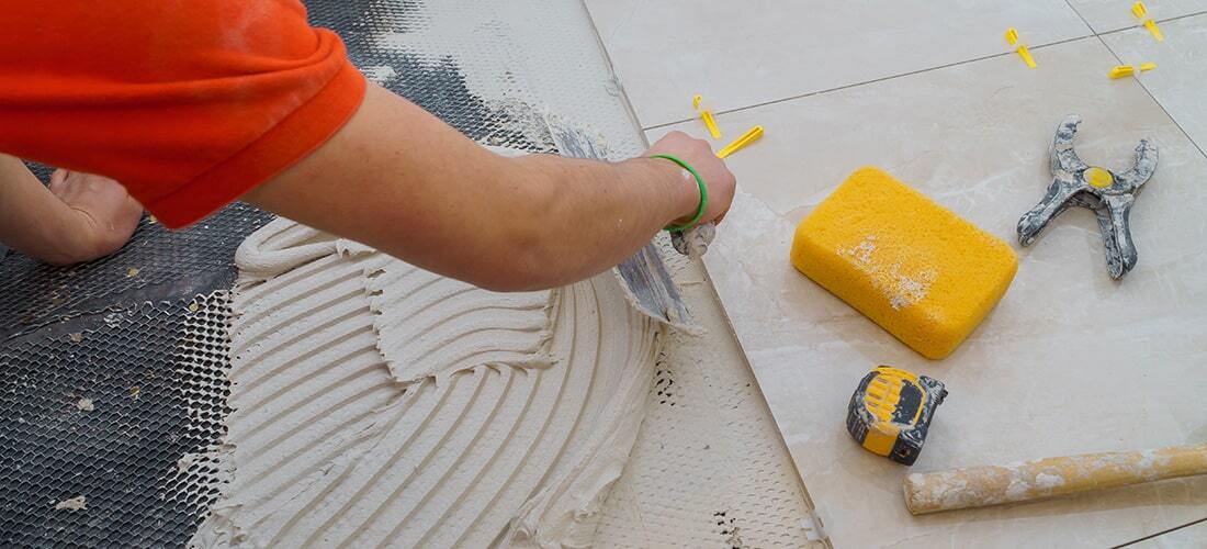 Worker installing floor tiles with yellow spacers.