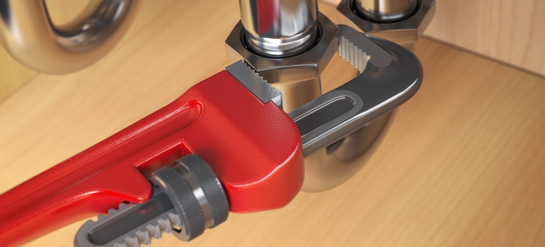 Plumbing using an adjustable wrench to repair pipework under a sink.