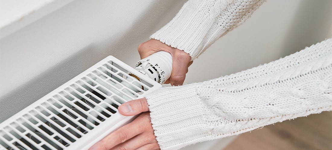 Homeowner in long sweater warming up hands on a radiator.